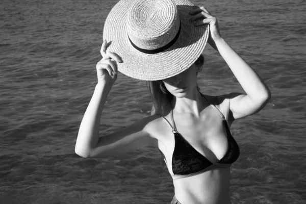 Black and white portrait of woman in bikini holding straw hat