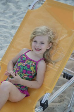 Kumsalda güneşli bir yatakta oturan sevimli bir kız. Mutlu yaz çocukluğu konsepti.