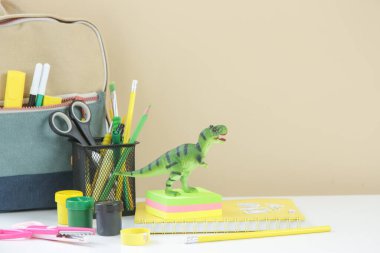 Eğitim ve okul kavramı: sırt çantası, okul kırtasiyeli not defterleri ve masada yeşil dinozor oyuncağı.