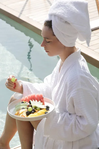 목욕하는 여자는 수영장 옆에서 과일을 먹으며 아름다운 아침을 즐기고 — 스톡 사진