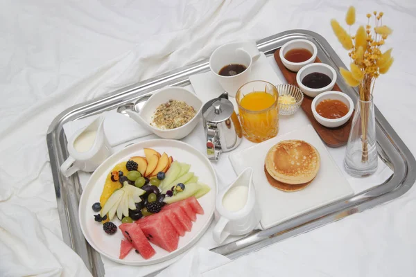 Breakfast tray in bed in luxury resort. Breakfast in bed with fruits, pancakes, cereals, coffee and juice on a tray.