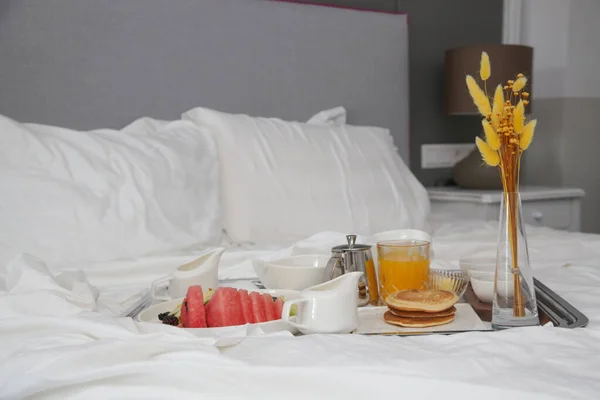 Breakfast tray in bed in luxury resort. Breakfast in bed with fruits, pancakes, cereals, coffee and juice on a tray.