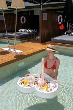 Yüzme havuzunda kalp şeklinde tepside yüzen lezzetli bir kahvaltısı olan genç bir kadın. Lüks tropikal tatil.