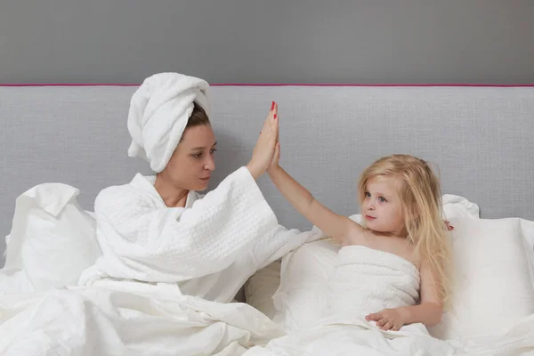 Mother and daughter high fiving on bed. Happy family time concept.