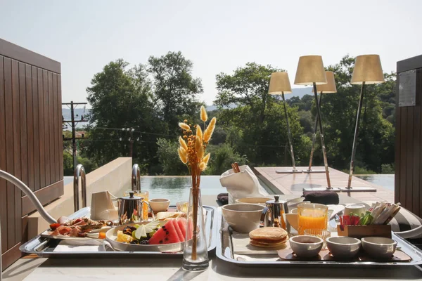 Breakfast tray with various choice of food and beverages on the table by the pool