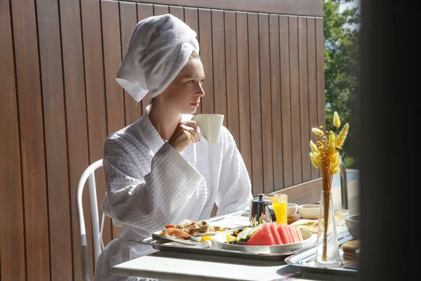 プールサイドのバルコニーで朝食と朝のコーヒーを楽しむ若い女性 — ストック写真