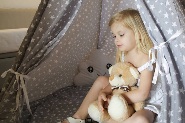 Милая малышка сидит в вигваме со своим плюшевым мишкой в спальне
