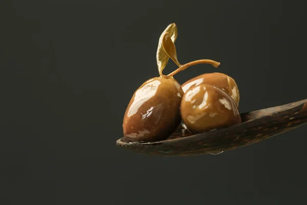 Extra virgin olive oil flows on a wooden spoon full of green olives against black background.