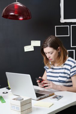 Cep telefonunu kontrol laptop önünde genç kadın
