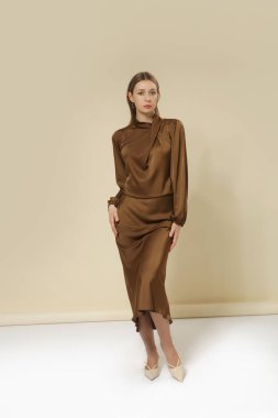Uzun kollu kahverengi ipek bluz giyen, kıvrılmış Drape Neck ve alevlenmiş maksimum etekli kadın model. Asgari monokrom zarif moda. Stüdyo çekimi.