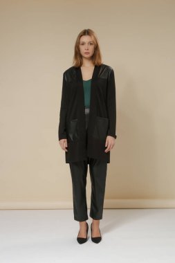 Stüdyoda çekilen fotoğraflarda şık günlük kıyafetler, yeşil pamuklu uzun gömlek, pamuk derili kombinasyon hırka ve siyah deri pantolon giyiliyor.