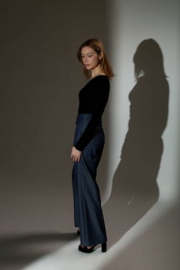 Uzun kollu beyaz ipek bluz giyen, kıvrık boyunlu ve yüksek bel pantolon giyen kadın model.