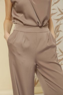 Stüdyo fotoğrafları. İpek bej bluz ve geniş paça pantolon giyen genç bir kadın model.