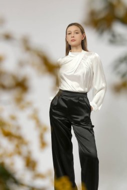 Uzun kollu beyaz ipek bluz giyen, kıvrık boyunlu ve yüksek belli siyah saten pantolon giyen kadın model, klasik iş stili.