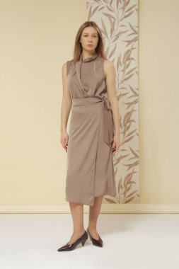 Bej renkli ipek bluz ve sarılı midi etek giyen bir kadın model. Şık ve zarif monokrom yaz kıyafeti. Moda Stüdyosu çekimi.