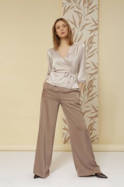 Stüdyo fotoğrafları. İpek bej bluz ve geniş paça pantolon giyen genç bir kadın model.
