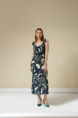 Tropikal yaprak desenli kolsuz elbise giymiş genç bir kadının seri fotoğrafları. Gündelik ve şık yaz kıyafetleri, bahar-yaz moda koleksiyonu.
