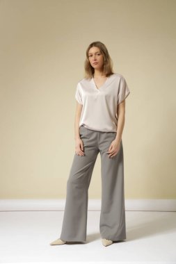 Açık gri, şık, gündelik, yüksek kaliteli pantolon ve V yaka beyaz bluz giyen kadın model. Zarif, basit bir iş görünüşü. Stüdyo çekimi.