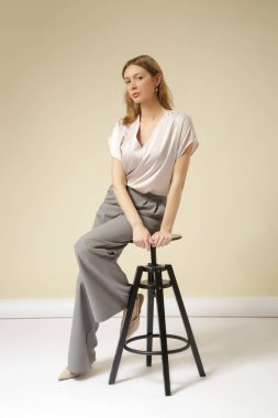 Açık gri, şık, gündelik, yüksek kaliteli pantolon ve V yaka beyaz bluz giyen kadın model. Zarif, basit bir iş görünüşü. Stüdyo çekimi.