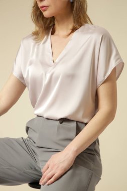 Açık gri, şık, gündelik, yüksek kaliteli pantolon ve V yaka beyaz bluz giyen kadın model. Zarif, basit bir iş görünüşü. Stüdyo çekimi.