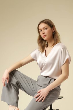 Açık gri, şık, gündelik, yüksek kaliteli pantolon ve V yaka beyaz bluz giyen kadın model. Zarif, basit bir iş görünüşü. Stüdyo çekimi.