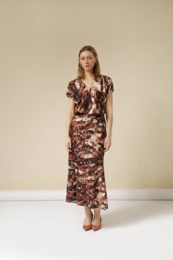 Soyut desenli kahverengi ipek midi elbiseli genç bir kadın modelin seri fotoğrafları..