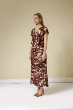 Soyut desenli kahverengi ipek midi elbiseli genç bir kadın modelin seri fotoğrafları..