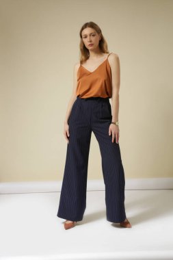 Lacivert çizgili beyaz çizgili, kahverengi Cami bluzlu, yüksek katlı bir pantolon giyen kadın model. Stüdyo çekimi.