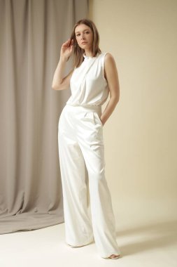 Beyaz saten geniş pantolon ve beyaz papyon yaka bluz giyen kadın modelin stüdyo fotoğrafı..