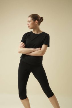 Temel siyah pamuklu tişörtlü ve dörtte üçlük kesilmiş taytlı bir kadın model..