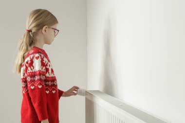 Çocuğun eli radyatör termostat vanasını ayarlıyor, merkezi ısıtma sistemini kontrol ediyor