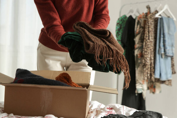 Spring Cleaning Organization, Decluttering, Moving and Donation Concept  Woman Sorting and Packing Clothes into Cardboard Box at Home