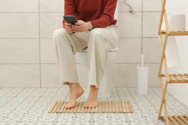 Tuvalette oturan kadın mide ağrısı, kabızlık ve ishal şikayetiyle cep telefonu kullanıyor.