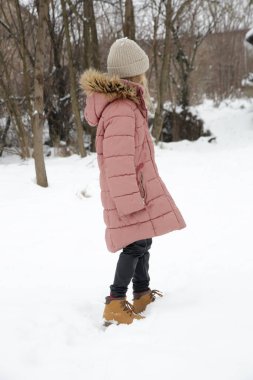 Açık havada, sevimli 8 yaşında, yün şapka ve pembe ceket giyen bir kızın portresi.