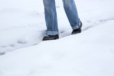 Kayma tehlikesi. Karlı buzlu yolda yürüyen tıknaz, deri çizmeli bir adam.