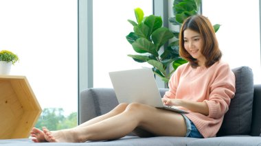 Evden çalışmak, ev bilgisayarında dizüstü bilgisayarla çalışan Asyalı bir kadın, çevrimiçi Asya bayan alışverişi, internetten öğrenen mutlu bir kız, online eğitim, ticaret sektörü, insan teknolojisi.