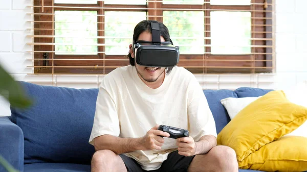 Asian man wearing virtual reality, VR headset at home living room,  Happy asia male with vr glasses playing video games with virtual reality headset and trying to touch something with hand, Stay at home