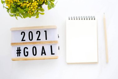 Ahşap kutu ve beyaz mermer zemin üzerine boş defter kağıdı üzerine 2021 hedef, yeni yıl iş başarısı hedefliyor
