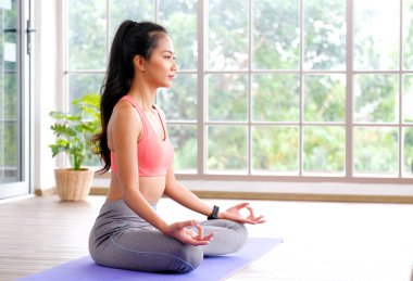 Asyalı kadın evde yoga meditasyon egzersizi yapıyor, genç Asyalı kadın rahat yoga pozisyonu için mindere oturuyor, evde egzersiz yapıyor, refah, akıl sağlığı...