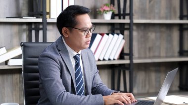 Asyalı iş adamı dizüstü bilgisayarla boğuşuyor, Asyalı adam ofiste çalışırken bilgisayara bakıyor, iş adamları teknolojiyle boğuşuyor. 