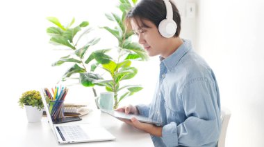 Video konferansı, evden çalışma, Asyalı bir adamın dijital tableti elinde tutarken iş adamlarına video görüşmesi, evdeki dizüstü bilgisayarla iş arkadaşlarıyla iletişim kurması.