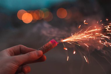 Genç adam açık havada fişek yakıyor.
