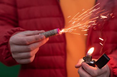 Kırmızı ceketli adam elinde havai fişek yakıyor.