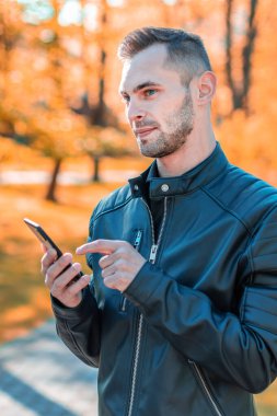 Autumn Park 'ta akıllı telefon kullanan yakışıklı adam.