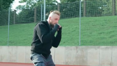 Genç Sakallı Adam dışarıda boks antrenmanı yapıyor.