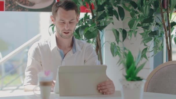 Cliente jovem faz chamada de vídeo em um café usando Tablet PC — Vídeo de Stock