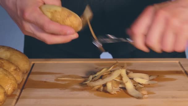 El hombre está pelando patatas en una cocina — Vídeo de stock