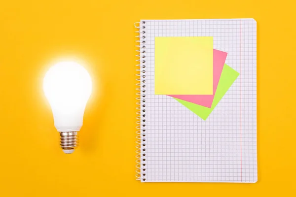 Glödande energisparande lampa och en anteckningsblock med klibbiga anteckningar — Stockfoto