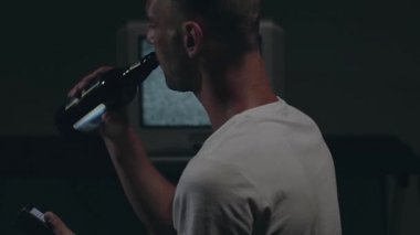 Beyaz tişörtlü adam Eski Gümüş TV karşısında oturuyor.