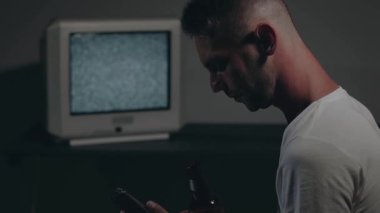 Beyaz tişörtlü adam Eski Gümüş TV karşısında oturuyor.